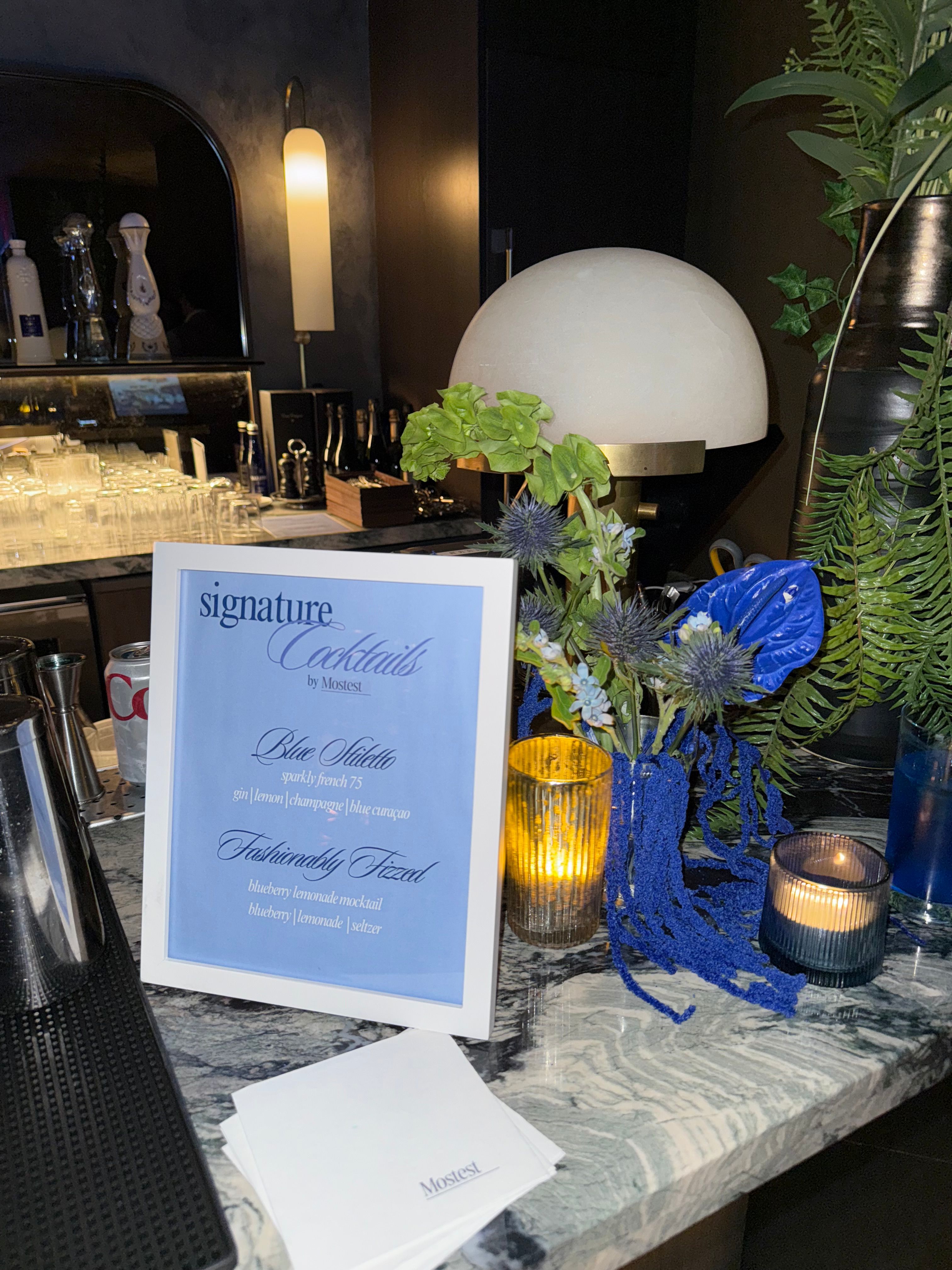 Something Blue signature cocktail menu by Mostest with blue florals and candlelight at the NEXUS Club bar.